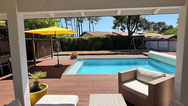 Un'area esterna coperta con piscina, mobili in vimini e un ombrellone giallo.