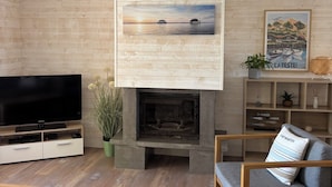 Un soggiorno moderno con una televisione a schermo piatto, un camino, pavimento in legno e un grande quadro sopra il camino.