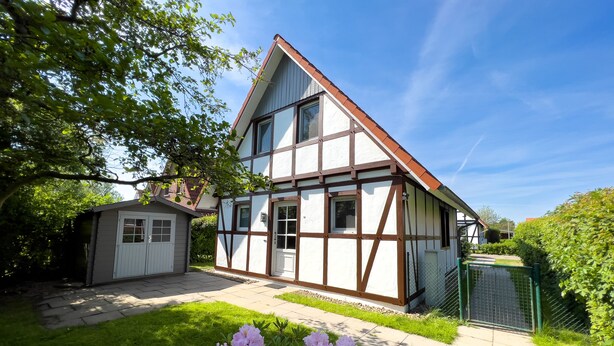 A two-story house with a gabled roof, a front garage, and a well-maintained lawn with pink flowers.