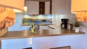 A kitchen with white cabinets, a wooden countertop, a coffee maker, a kettle, and a potted plant.
