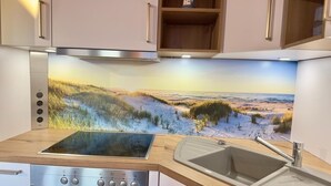 A kitchen with a built-in stove, oven, and sink, featuring a scenic wallpaper backsplash.