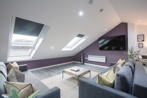 A modern living room with a sloped ceiling, skylights, a flat-screen TV, and a grey sofa.