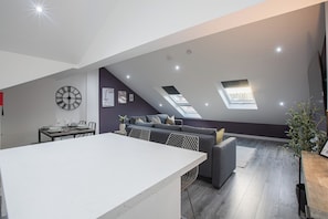 A modern loft with a dining area, a sofa, and a skylight.