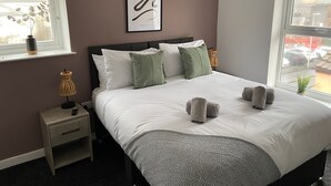 Et soveværelse med en seng, sengeborde, en lampe, et indrammet kunstværk og udsigt gennem vinduet.