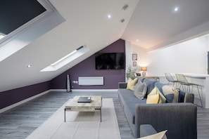 A modern living room with a sloped ceiling, a sofa, a coffee table, and a TV mounted on the wall.