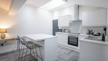 Cozinha moderna com armários brancos, uma ilha central com banquetas, forno embutido e claraboia.
