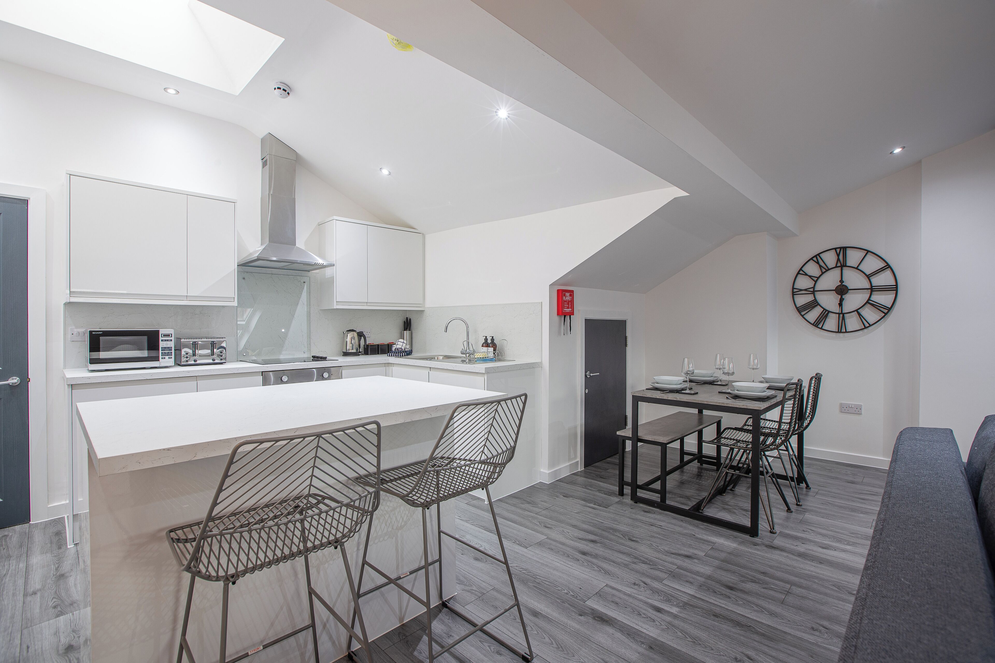 Een moderne keuken met een centraal eiland, barkrukken, een eettafel met stoelen en een wandklok.