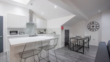 Een moderne keuken met een centraal eiland, barkrukken, een eettafel met stoelen en een wandklok.