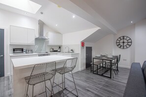 A modern kitchen with a central island, bar stools, a dining table with chairs, and a wall clock.