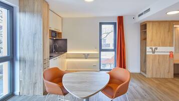 Una cocina moderna con armarios de madera, microondas y fregadero. Hay una zona de comedor con una mesa y dos sillas naranjas.