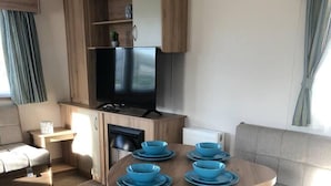 A compact living space with a kitchenette, a dining table with blue plates, a sofa, and a television.