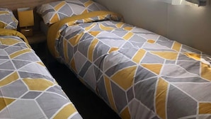 A single bedroom with a wooden headboard, a window with curtains, and two beds with matching bedding.