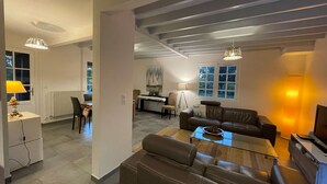 Uma sala de estar moderna com um sofá de couro, uma mesa de centro de vidro e uma área de jantar com mesa e cadeiras.
