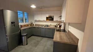 Cozinha moderna com armários cinza, geladeira de aço inoxidável e janela com vista para árvores.