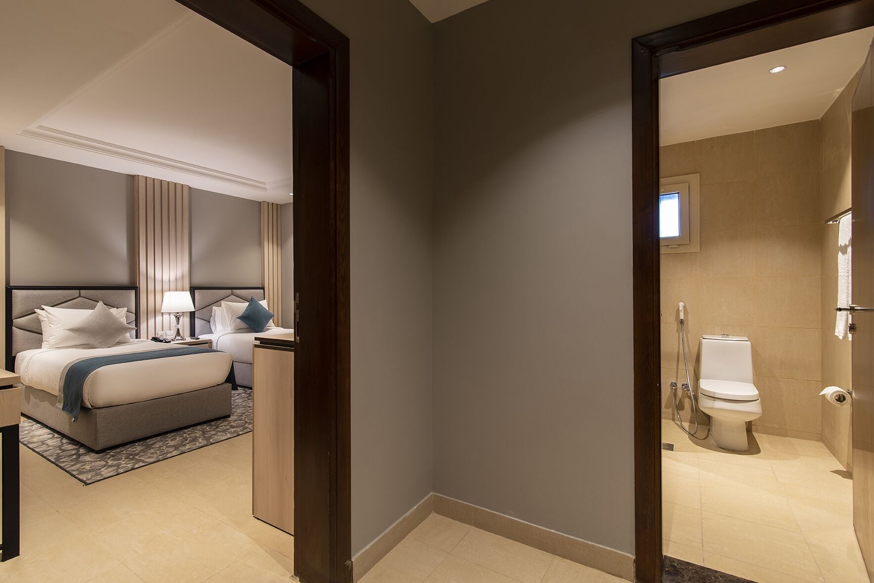 A hotel room with a bed, bedside tables, a nightstand, a mirror, and a bathroom with a toilet and shower.