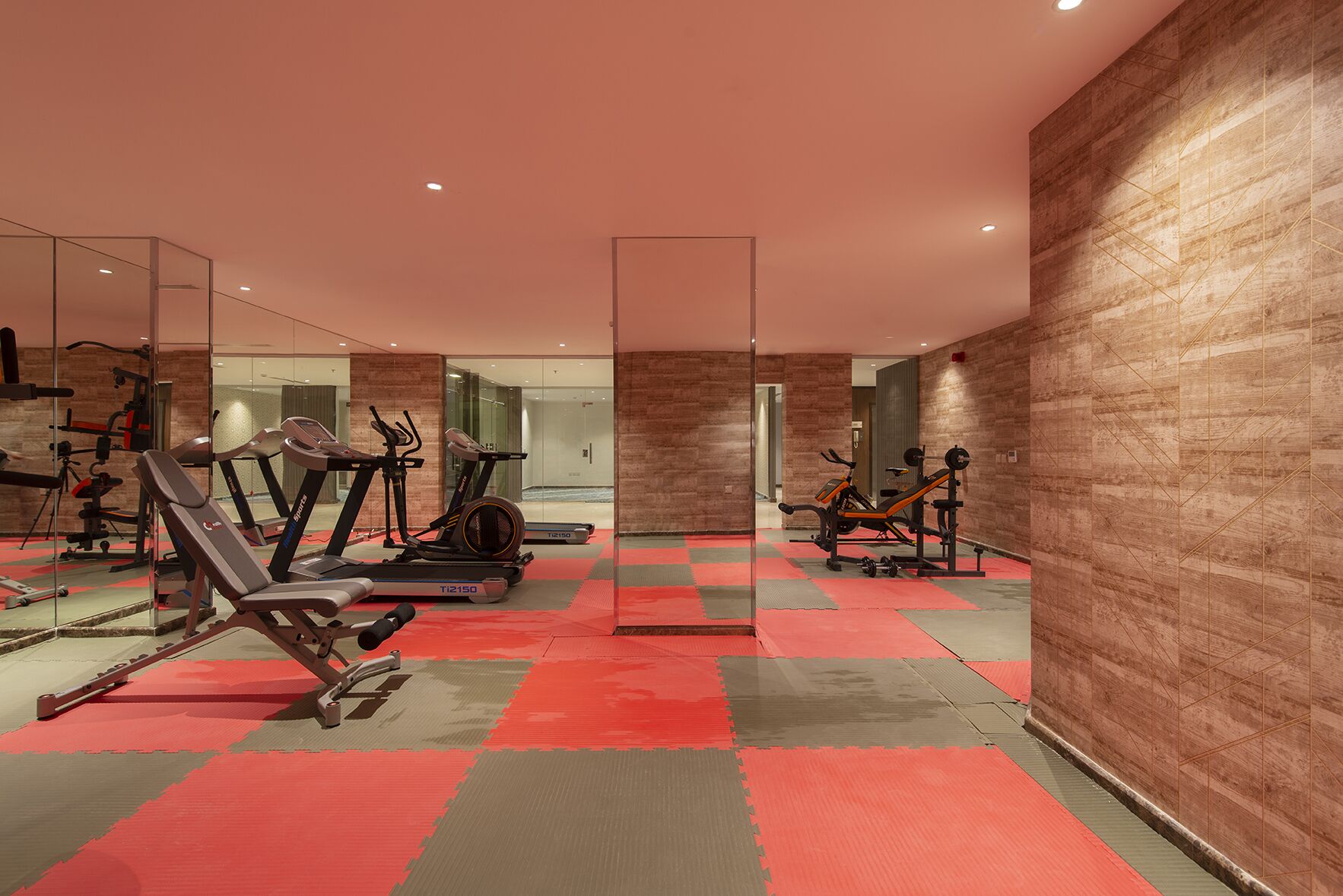 Un gimnasio moderno con equipo de ejercicio, paredes con espejos y suelo a cuadros.