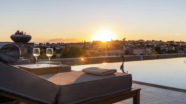 A rooftop pool with lounge chairs, a sunken seating area, and a view of a cityscape during sunset. - Akrolithos luxury suites (Nea Propontida)
