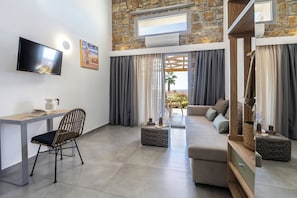 Ein modernes Wohnzimmer mit Fernseher, Sofa, Sessel und Schreibtisch.