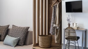 A modern room with a sofa, a wooden slat partition, a wicker basket, a chair, and a flat-screen TV mounted on the wall. - Akrolithos luxury suites (Nea Propontida)
