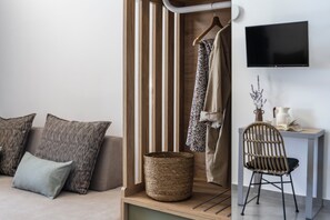 A modern room with a sofa, a wooden slat partition, a wicker basket, a chair, and a flat-screen TV mounted on the wall. - Akrolithos luxury suites (Nea Propontida)