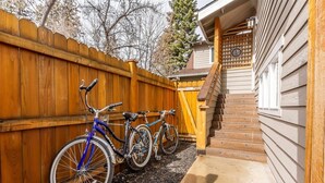A wooden fence with two bicycles parked against it, a concrete pathway, and a wooden staircase leading to a house with a 'GEND' sign.