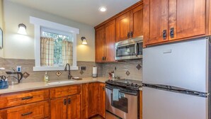 A kitchen with wooden cabinets, stainless steel appliances, a window with curtains, and a tiled backsplash.