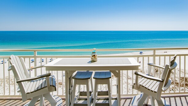 Una terraza con una mesa y dos sillas Adirondack con vista a una playa y una vista despejada del océano.