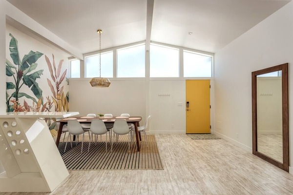 Bright dining area with vaulted clerestory windows, tropical mural, and mid-century table seating 8 — first impressions that set the desert mood