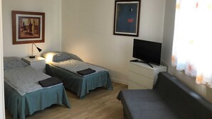 Ett rum med två enkelsängar, en TV, en soffa och en tavla på väggen.