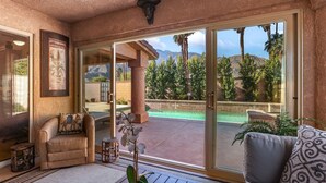 Une vaste terrasse offrant une vue sur une piscine et des montagnes, avec un coin salon confortable et une plante en pot.