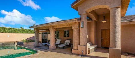 A house with a pool, outdoor seating, and a covered patio area.
