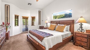 Une chambre spacieuse avec un grand lit, deux tables de chevet, un ventilateur de plafond et une fenêtre donnant sur un paysage verdoyant.