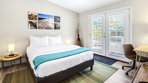 Ein Hotelzimmer mit einem Bett, zwei Nachttischlampen, einem Schreibtisch mit Stuhl und Blick durch die Tür.
