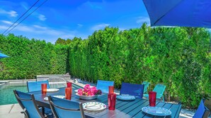 Ein Essbereich im Freien mit Pool, blauen Stühlen und einem Tisch, der mit Tellern, Tassen und Blumen gedeckt ist.