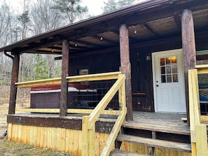 Un chalet rustique doté d’un porche en bois, d’un escalier et d’une porte avec une fenêtre.