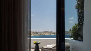 A balcony with a view of the sea, a small table with flowers, and a cushioned seating area. - Noima Boutique Hotel Mykonos (Mykonos)