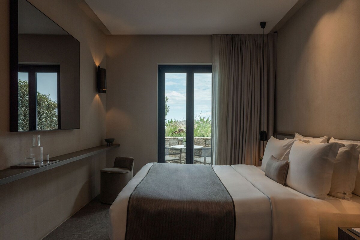 Une chambre d’hôtel équipée d’un lit, d’un bureau, d’une chaise, d’une grande fenêtre et offrant une vue sur l’extérieur.