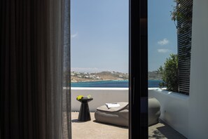 Un balcón con vista al mar, una mesa con una copa de bebida y un cojín.