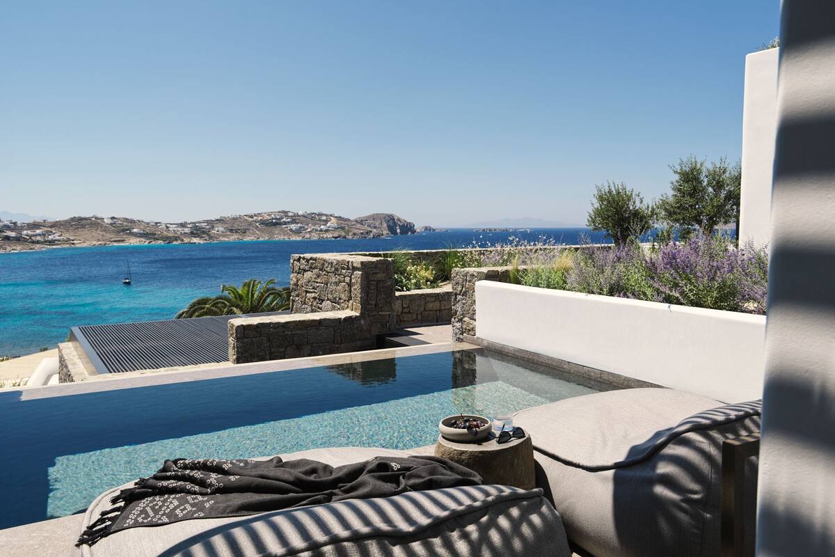 Blick auf einen Pool mit blauem Meer und weiter Küste im Hintergrund.