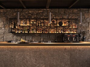 Een bar met een achtergrond van een stenen muur, flessen met drank en een koffieapparaat.