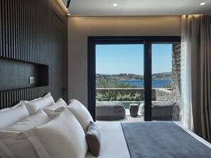 Un dormitorio moderno con una cama grande, vista al mar y un balcón con mobiliario exterior.