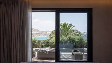 Ein Hotelzimmer mit einer großen Schiebeglas-Tür, die auf einen Sitzbereich im Freien mit Blick auf das Meer und die Hügel führt.