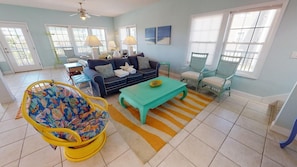 A spacious living room with a blue sofa, a yellow rocking chair, and a teal coffee table. - Lowest priced home in Seagrass 350 steps to Gulf with community pool access (Port St. Joe)