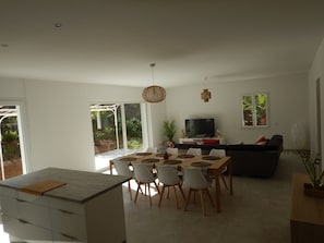 A modern living space with a dining area, a sofa, a TV, and a large window overlooking greenery. - LARGE VILLA (12 people) WITH A SWIMMING POOL, 5 MINUTES FROM THE BEACH (Six-Fours-les-Plages)