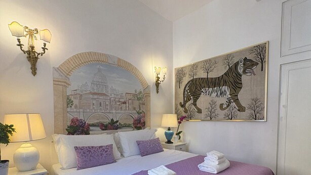 Quarto de hotel com uma cama grande, uma mesa de cabeceira com abajur, ar condicionado fixado na parede e um quadro de um tigre.