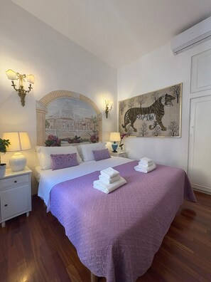 Una camera d'albergo con un letto grande, un comodino con una lampada, un condizionatore d'aria a muro e un quadro che raffigura una tigre.