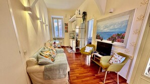 Uma sala de estar aconchegante com um sofá, cadeiras, uma TV e um quadro de uma paisagem.