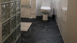 Un bagno con il water, uno spazio doccia in vetro e un pavimento in marmo.