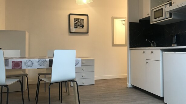 Una cucina moderna con mobili bianchi, un forno a microonde e un lavello. C'è un'area pranzo con tavolo e sedie.