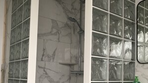 Un bagno con doccia, piastrelle in marmo e un mobile lavabo con specchio e una bottiglia verde.
